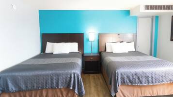 A hotel room with two beds, each with a headboard, a nightstand, and a wall-mounted lamp.