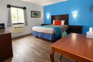Habitación de hotel con cama, mesitas de noche, escritorio, silla, ventana con cortinas, un cuadro en la pared y aire acondicionado de pared.