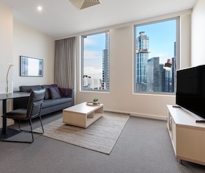 A modern living room with a sofa, coffee table, TV, and large windows offering a city view.