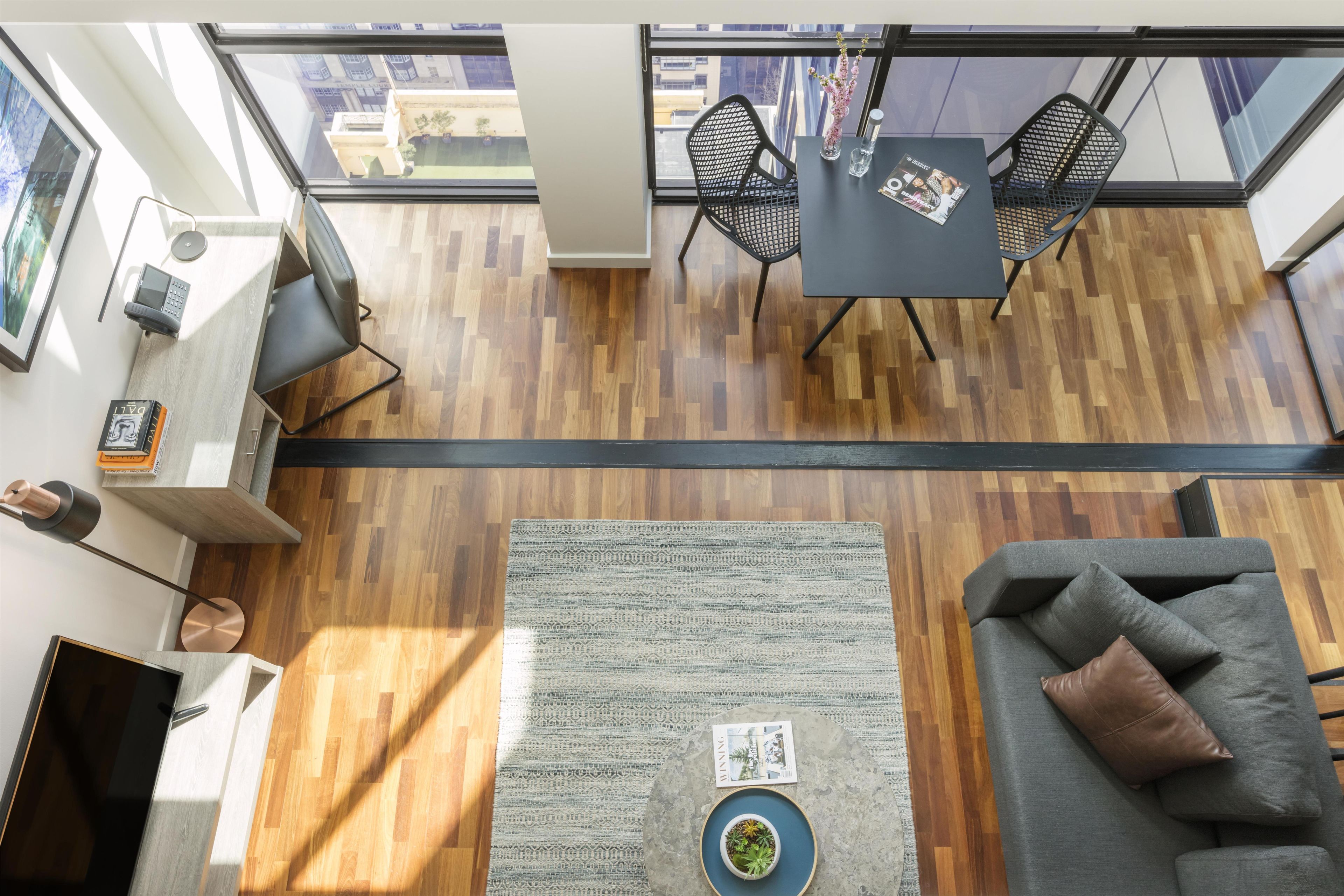 A modern living room with a wooden floor, a gray sofa, a coffee table, and a dining area with two chairs and a table.