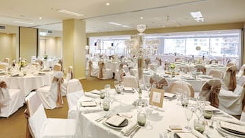 Un salón de banquetes con mesas redondas, manteles blancos y sillas con cintas marrones.
