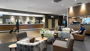 A modern hotel lobby with a reception desk, seating area, and a bar.