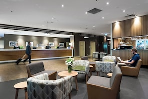 A modern hotel lobby with a reception desk, seating area, and a bar.