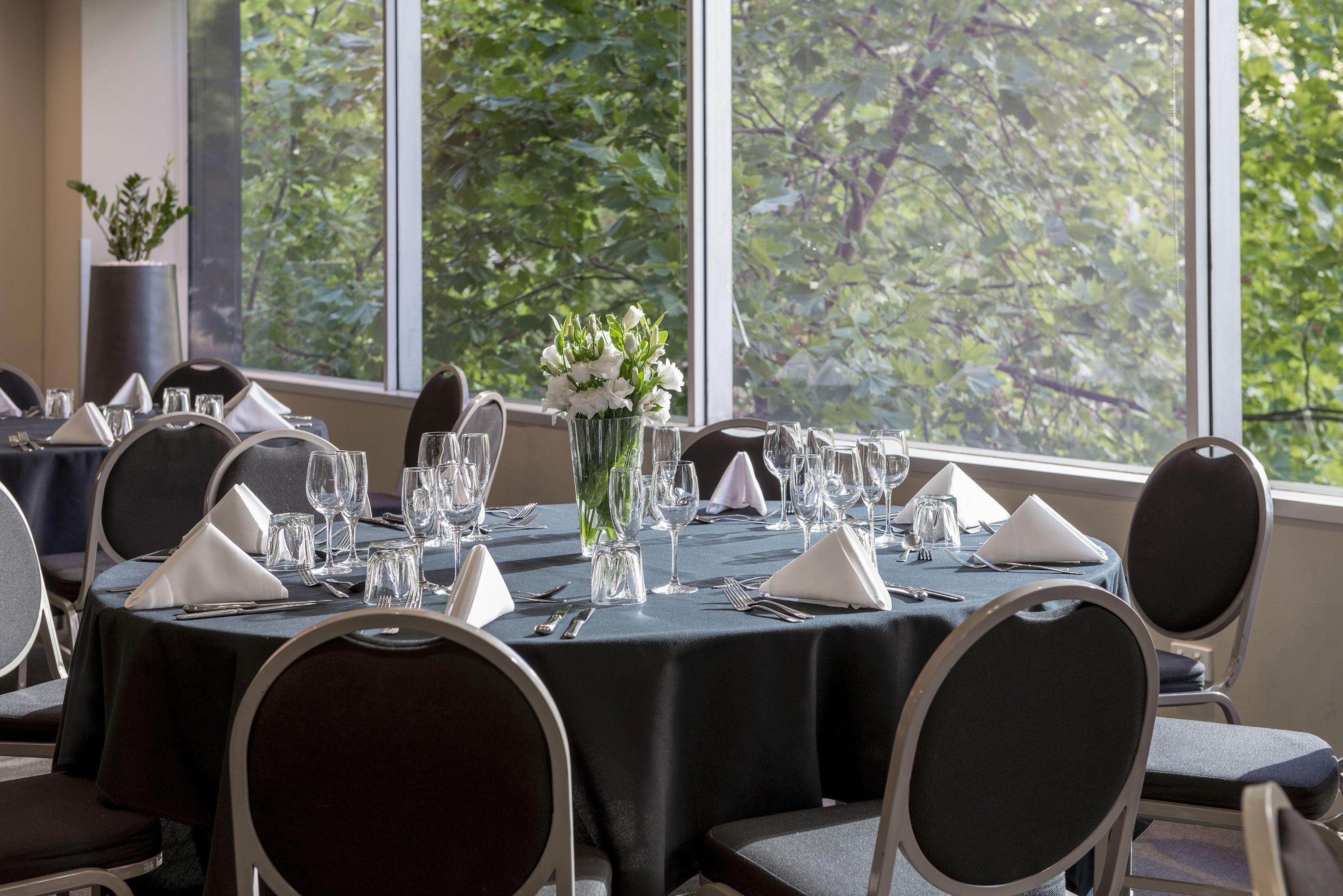A dining area with round tables set for a meal, chairs, and a vase of flowers.
