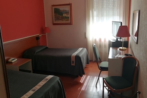 A hotel room with two beds, a desk, a chair, a TV, and a painting on the wall.