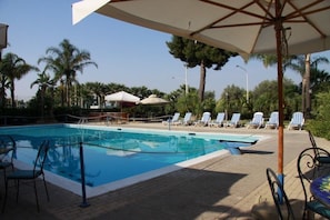 A swimming pool with lounge chairs and umbrellas, surrounded by palm trees.