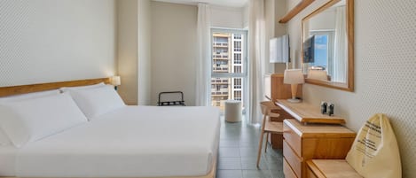 Habitación de hotel con cama, escritorio, silla, espejo y vistas al exterior.