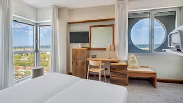 Habitación de hotel con una cama grande, un escritorio con silla, televisión y vista al mar.
