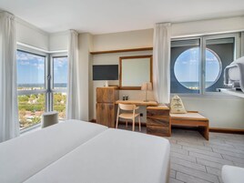 Habitación de hotel con una cama grande, un escritorio con silla, televisión y vista al mar.