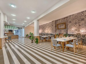 Un comedor con piso a rayas, mesas, sillas y una cocina al fondo.