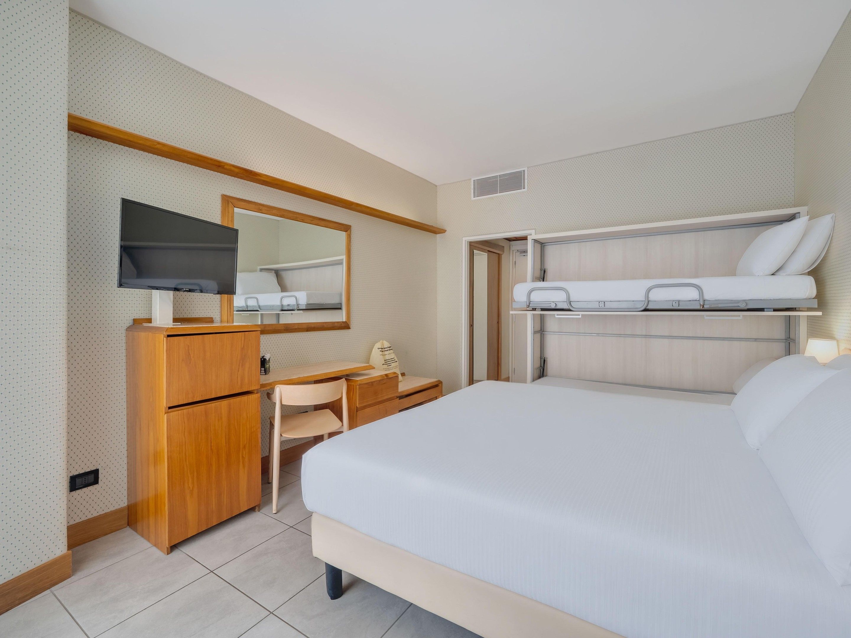 A hotel room with a bed, a desk, a chair, a television, and a mirror.