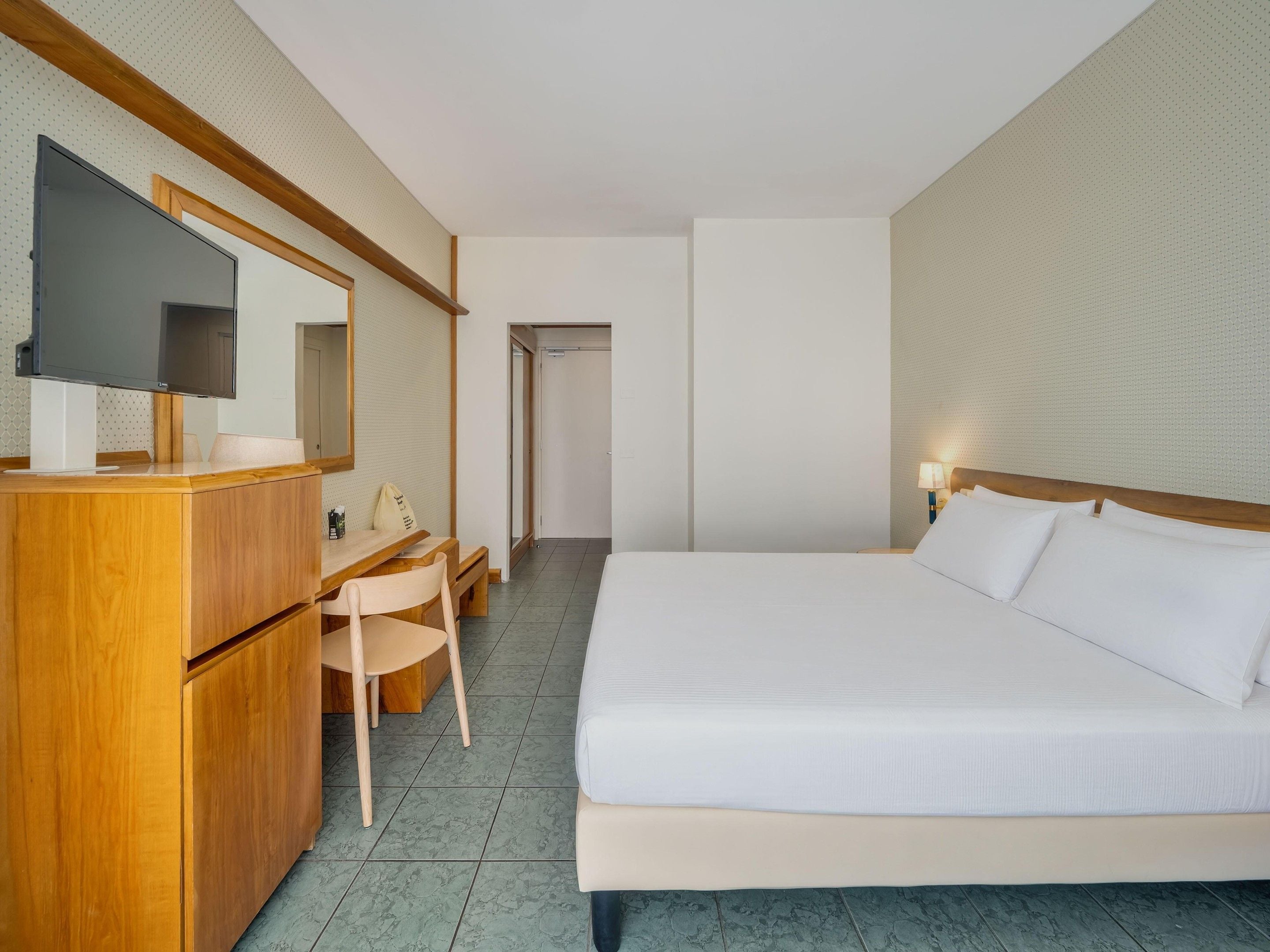 A hotel room with a bed, a desk with a chair, a television, and a mirror.