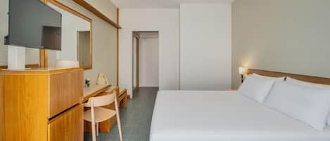 Une chambre d’hôtel comprenant un lit, un bureau avec une chaise, une télévision et un miroir.