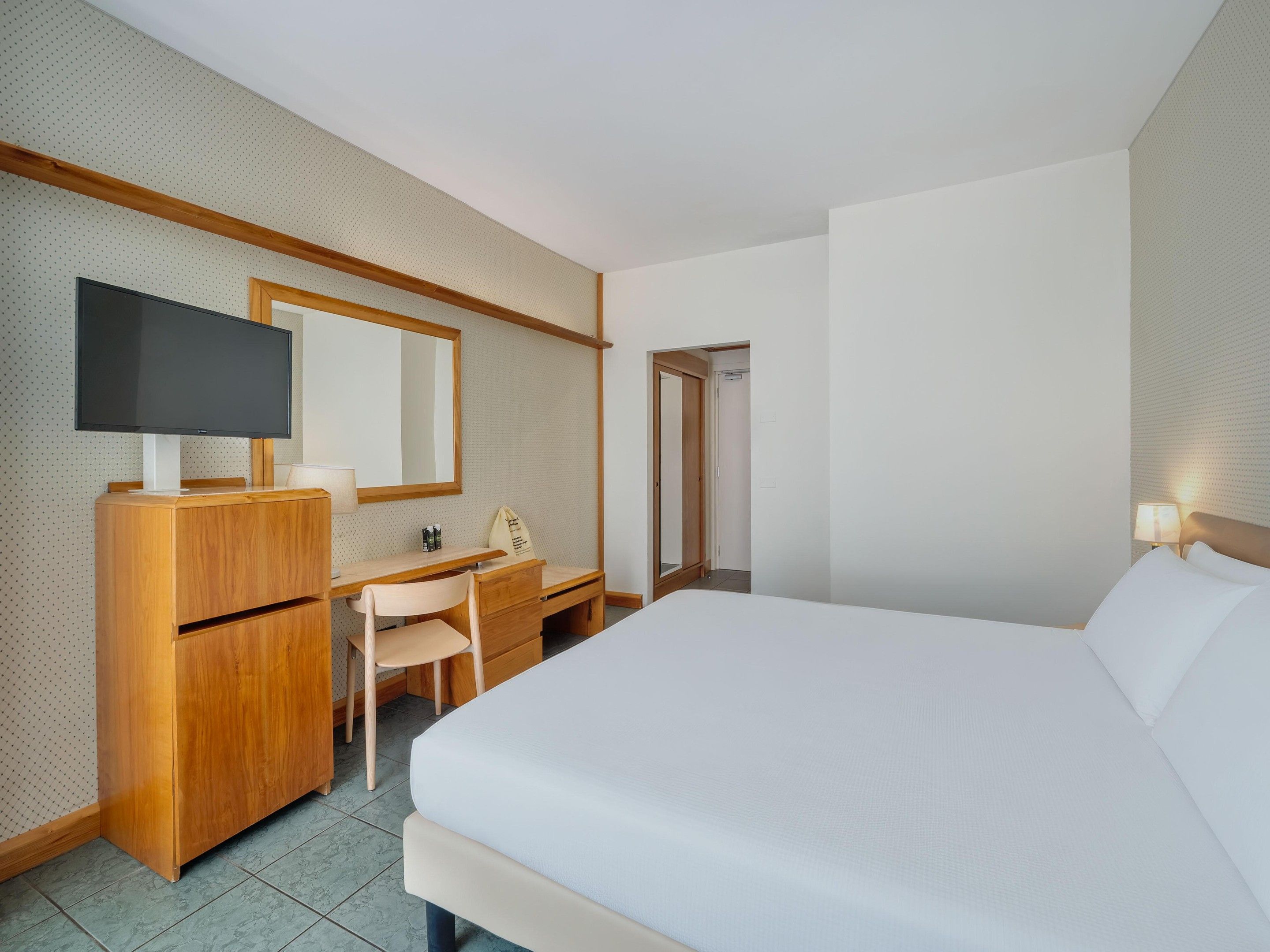 A hotel room with a bed, a desk, a chair, a television, and a mirror.