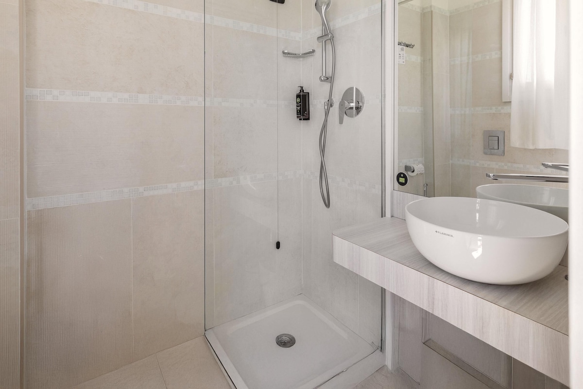 Un baño moderno con ducha envuelta en vidrio, un lavabo blanco y un espejo sobre él.