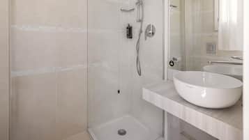 Un baño moderno con ducha envuelta en vidrio, un lavabo blanco y un espejo sobre él.