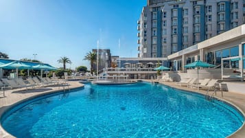 Un espace piscine d'hôtel avec des chaises longues, une fontaine et un bâtiment portant une enseigne.