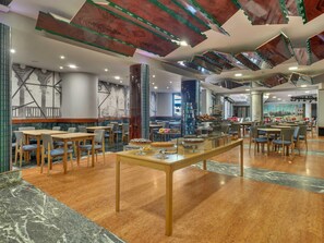 A spacious dining area with marble flooring, wooden tables, and chairs, and a central serving counter with desserts. - B&B Hotel Chioggia Airone (Chioggia)