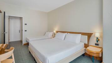 Quarto de hotel com uma cama grande, duas mesas de cabeceira com luminárias, uma cadeira de madeira e uma porta.