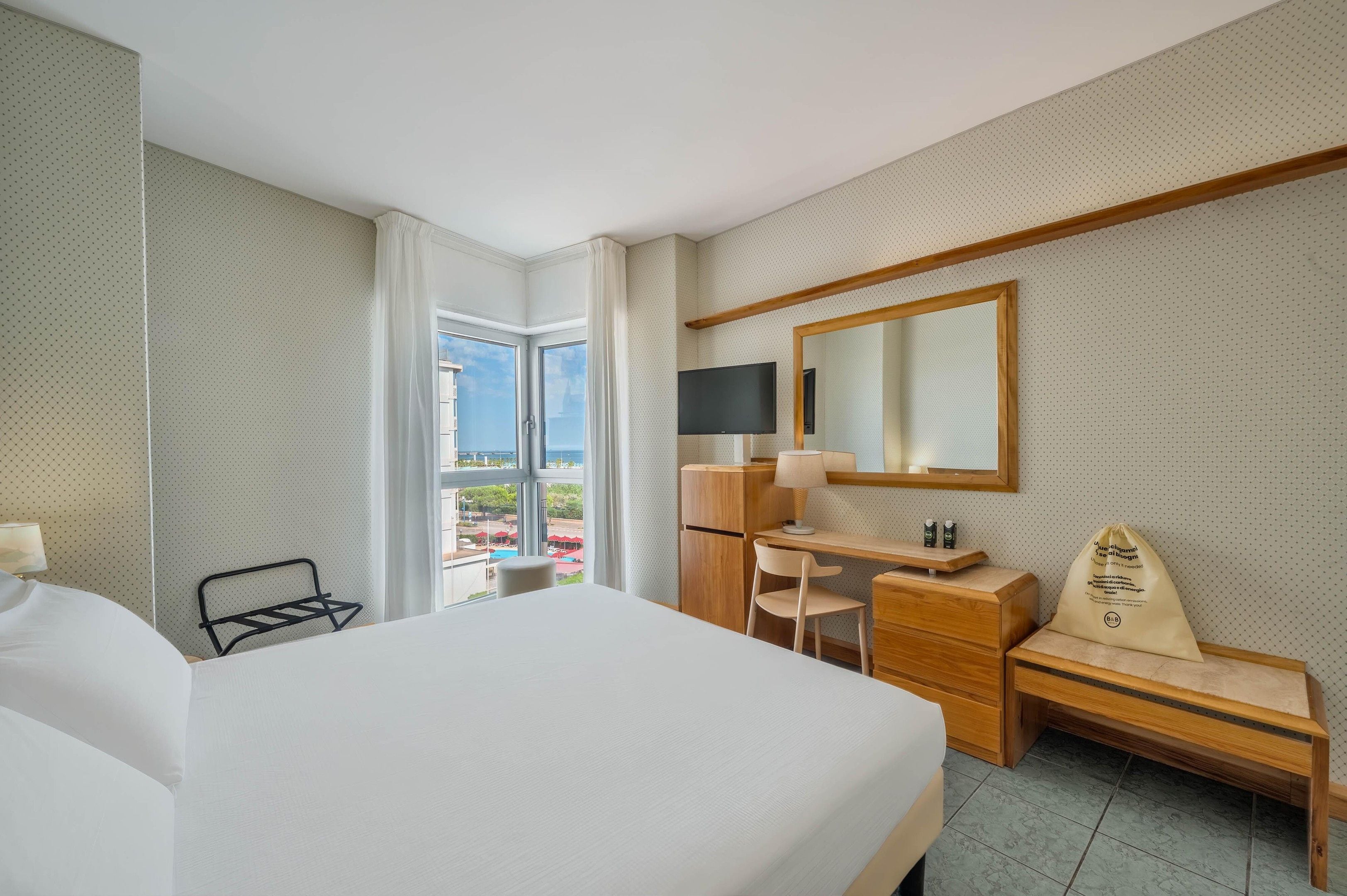 Une chambre d’hôtel équipée d’un lit, d’un bureau, d’une chaise et d’une grande fenêtre donnant sur un paysage agréable.