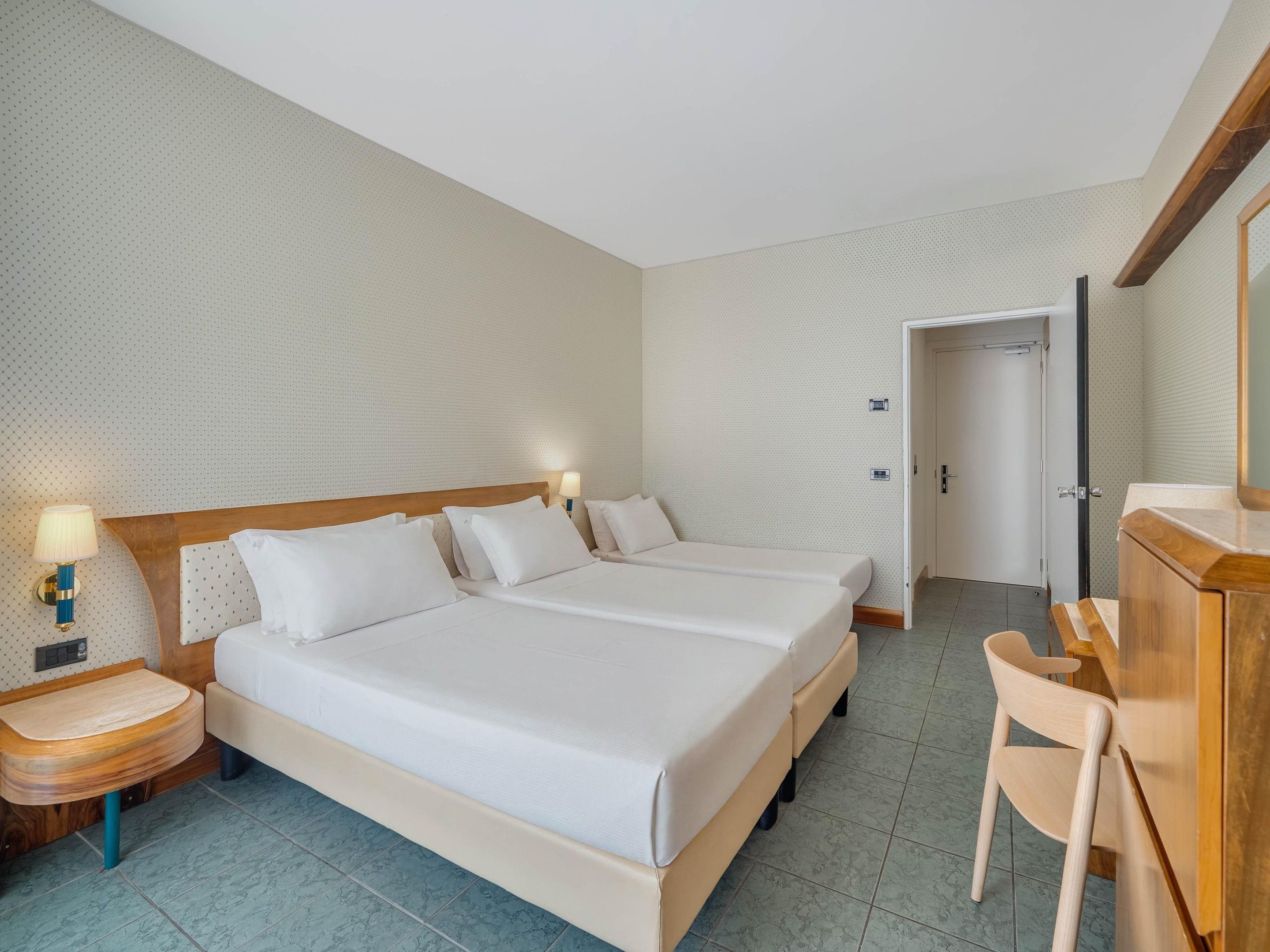 Een hotelkamer met een tweepersoonsbed, nachtkastjes, een bureau en een stoel.