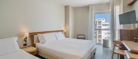 A hotel room with a large bed, a desk, a chair, a TV, and a balcony with a city view.