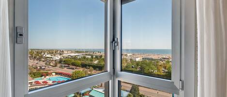 Ein Hotelzimmer mit großem Fenster, Blick auf einen Pool und einen Strand.
