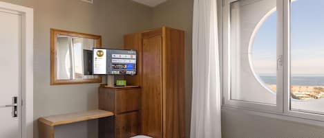 Habitación de hotel con cama, armario de madera, escritorio pequeño, televisor y ventana con vista al mar.