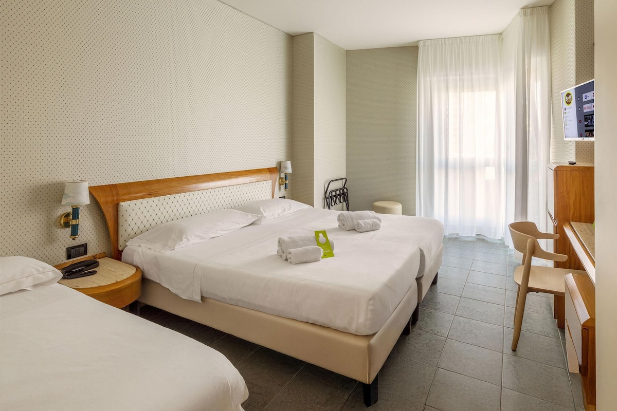 A hotel room with two beds, a desk, a chair, and a television on the wall.
