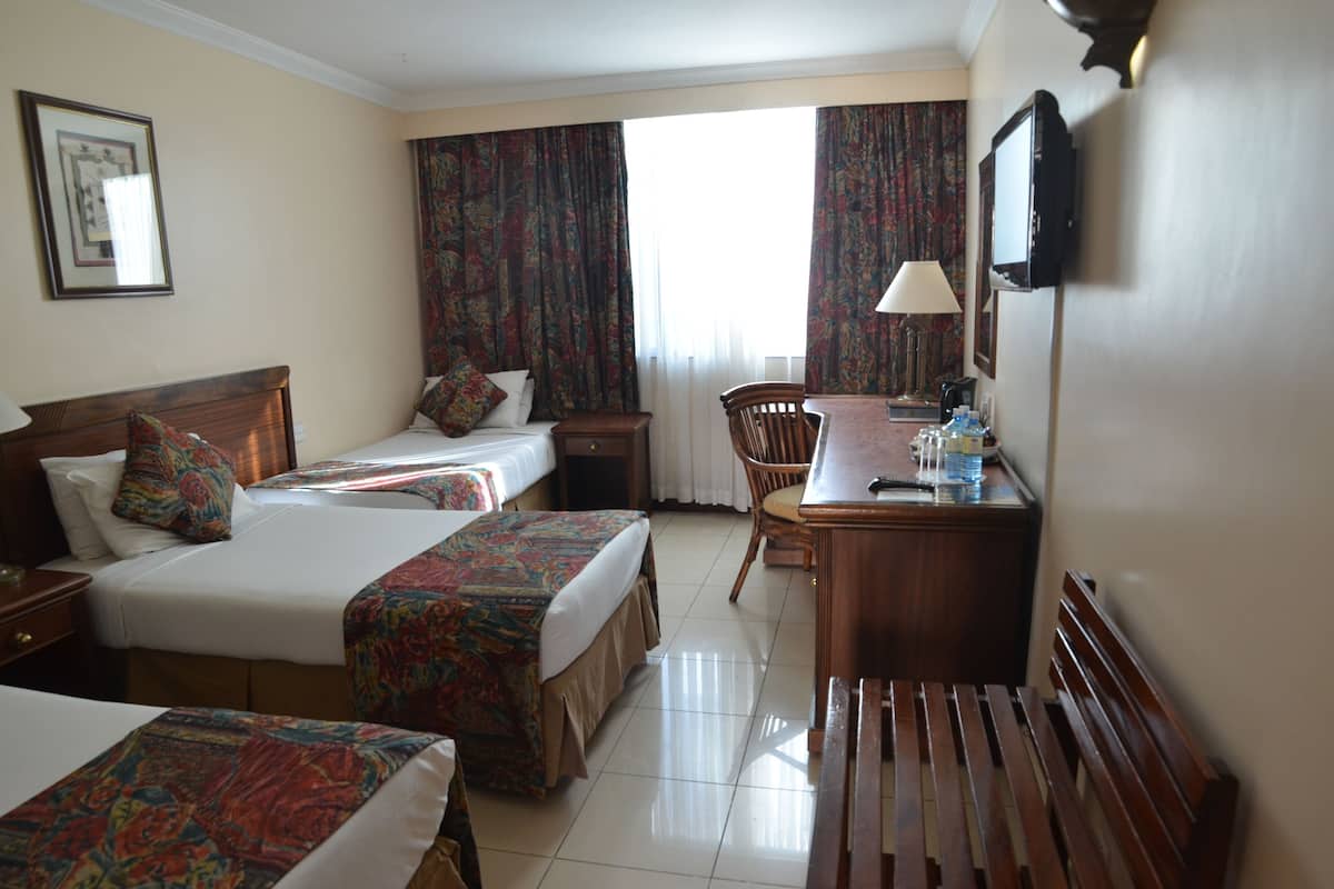 A hotel room with two beds, a desk, a chair, a television, and a window with curtains.