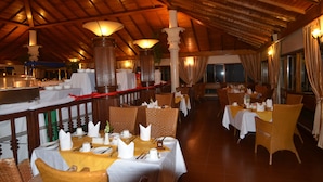 A restaurant with wooden ceiling beams, tables set with white tablecloths, and wicker chairs.