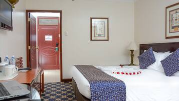 A hotel room with a bed, a desk with a laptop, a chair, and a door.