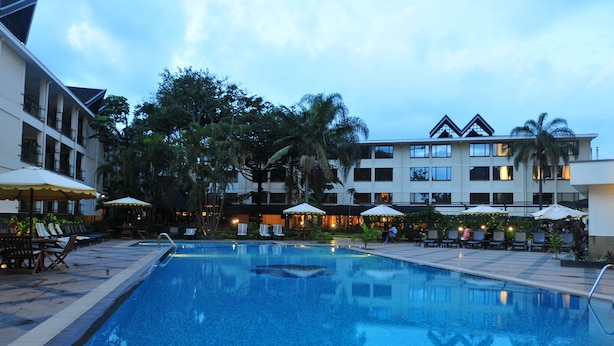 A swimming pool with lounge chairs and umbrellas, surrounded by buildings and trees.