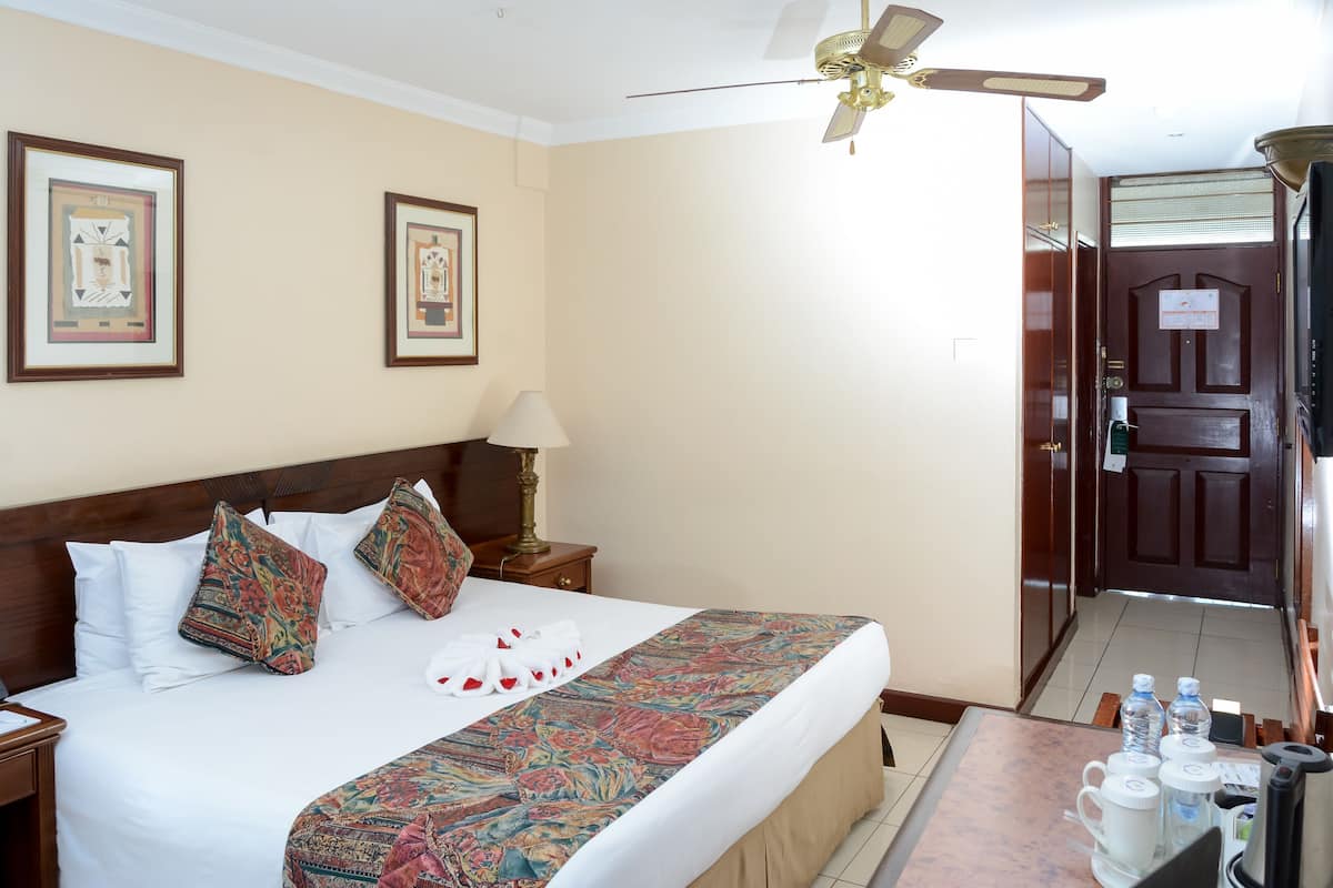 A hotel room with a bed, a nightstand, a lamp, a ceiling fan, and a door.