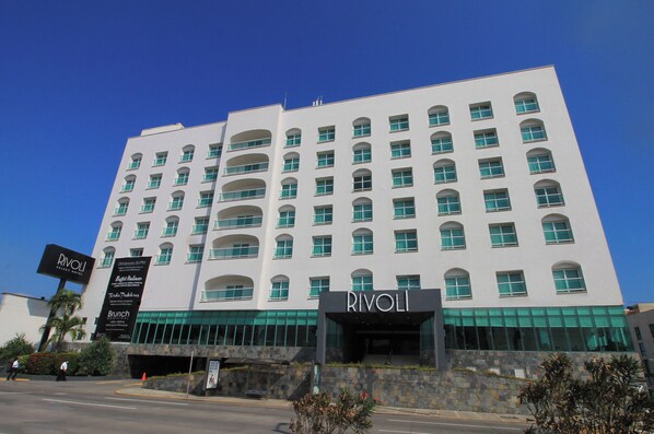 A multi-story hotel with a prominent 'Rivoli' sign at the entrance, featuring a modern architectural style with arched windows and a stone facade.