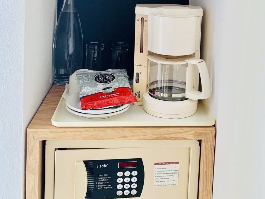 A coffee machine, a bottle of water, a coffee pod, and a small shelf with a pot labeled "RÍVOLJ SELECT HOTEL".