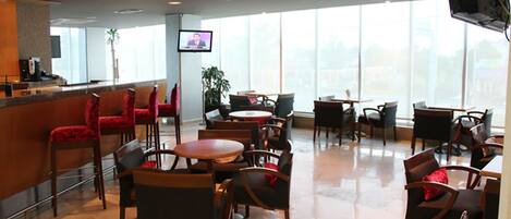 A hotel lobby with a reception desk, red and black chairs, round tables, and a large window providing a view of the city.