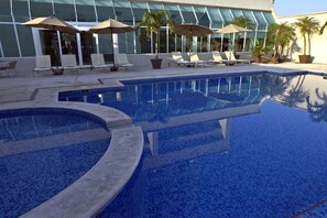 A pool area with lounge chairs and umbrellas, surrounded by a modern building with large windows.