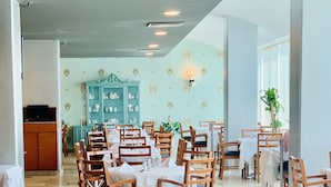 Een restaurant met meerdere tafels en stoelen, een blauwgroene kast en decoratieve wandlampen.
