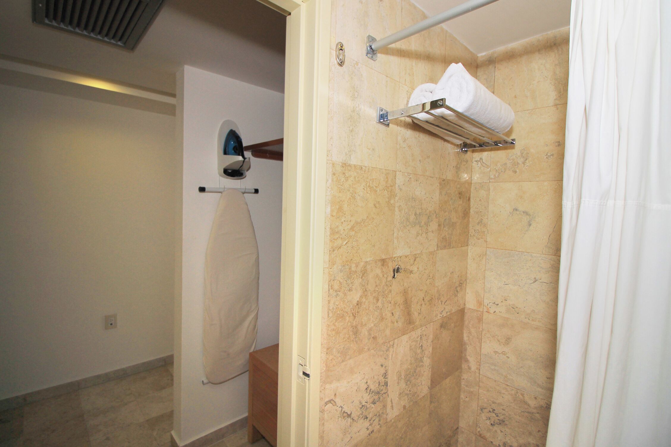 A bathroom with beige tiles, a towel rack, and a shower curtain.