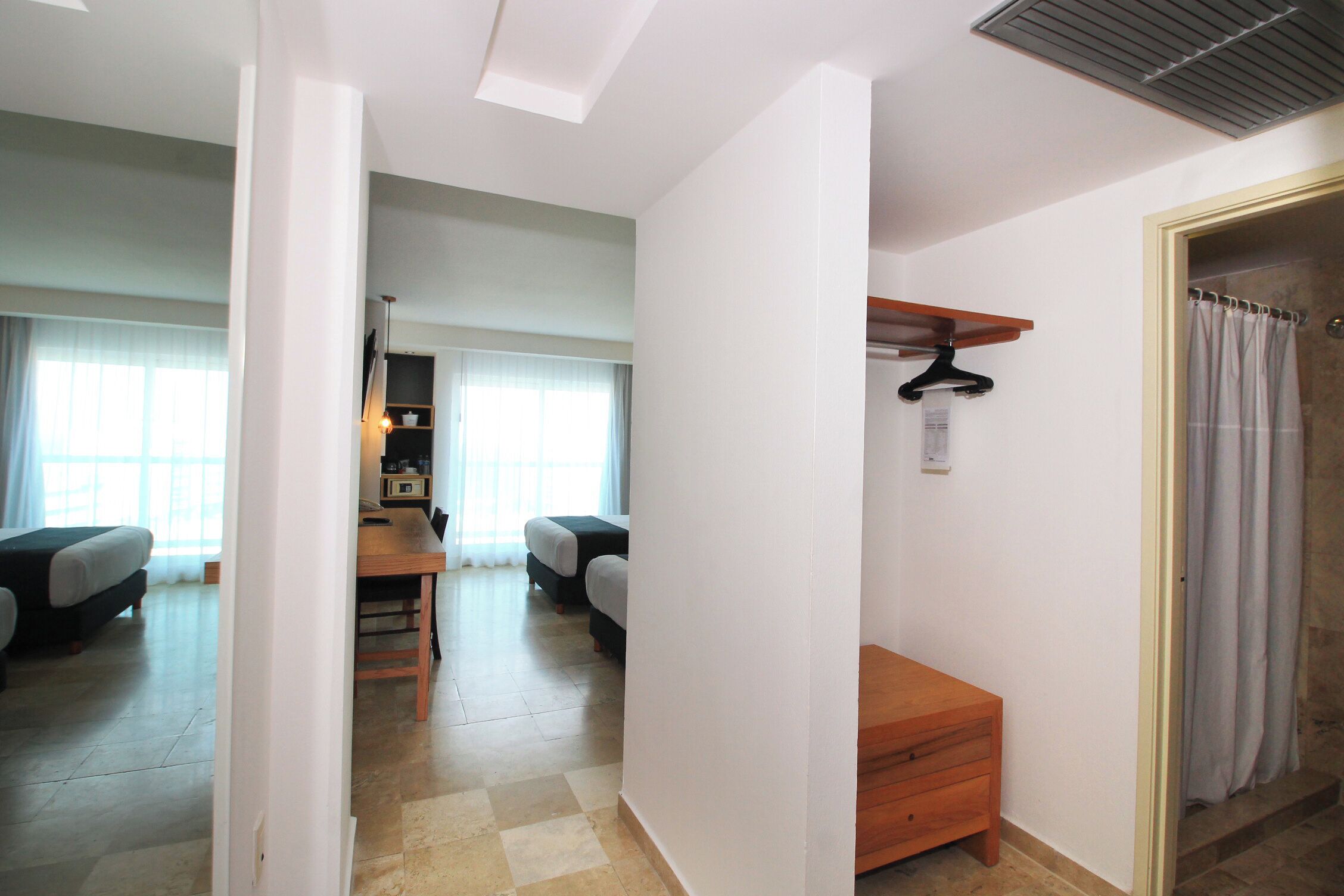 A hotel room with a bed, a wooden nightstand, a small table, and a bathroom with a shower curtain.