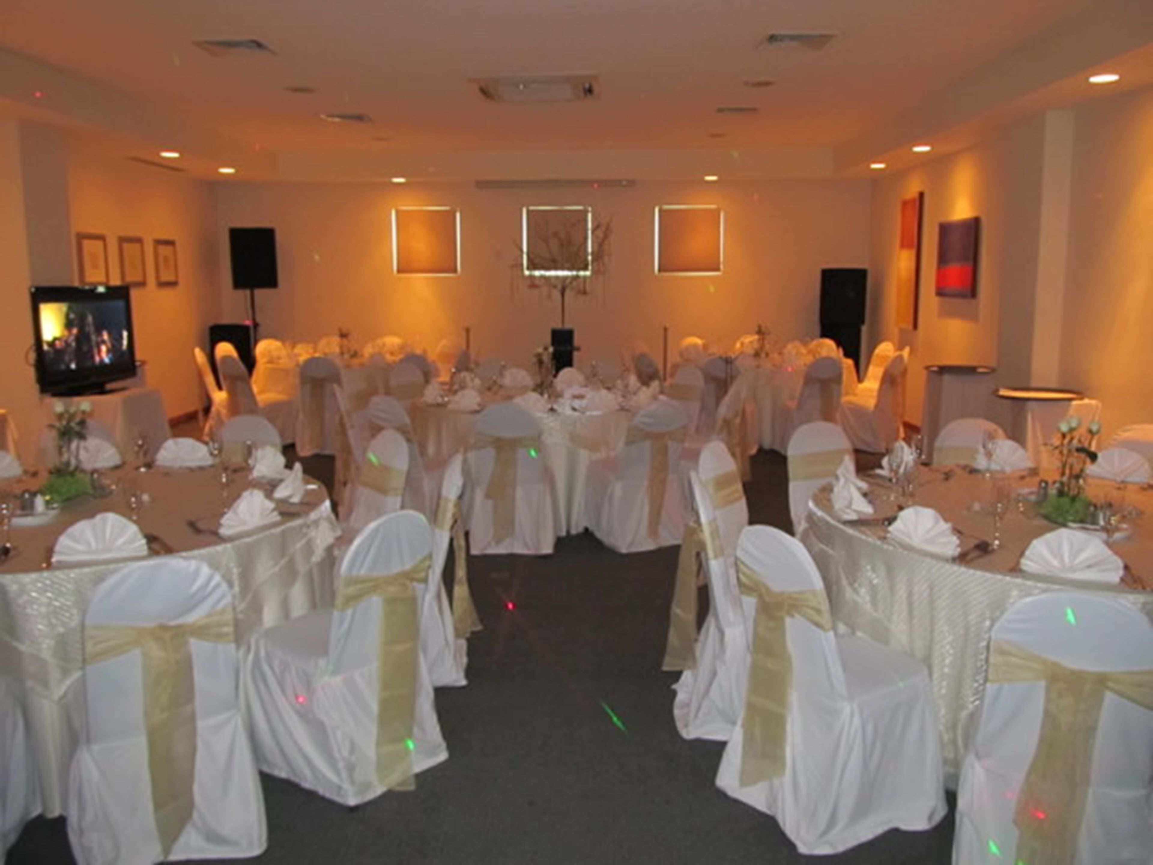 A banquet hall with round tables, white tablecloths, and chairs with white and gold sashes.