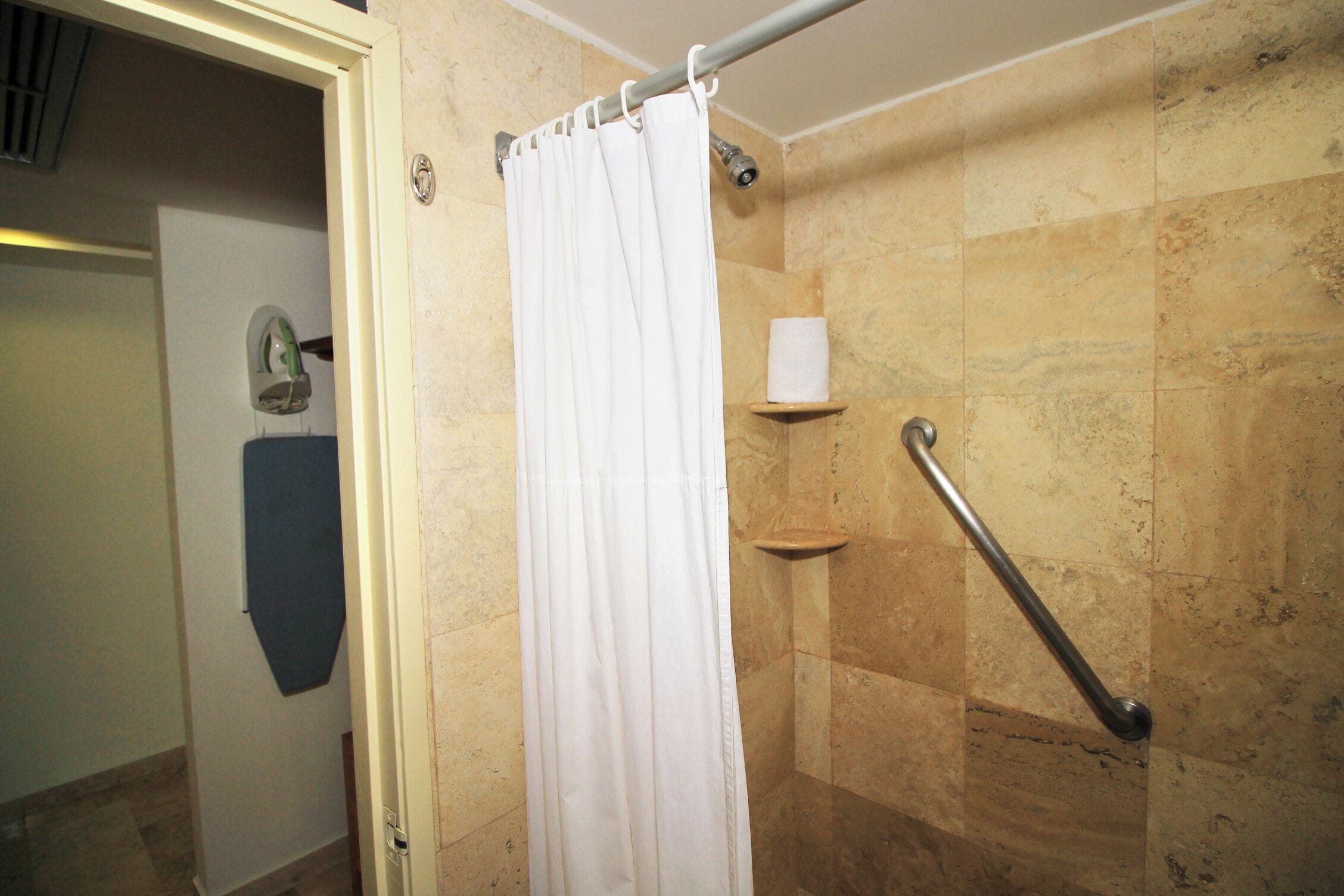 A bathroom with a shower curtain, a towel dispenser, and a grab bar.