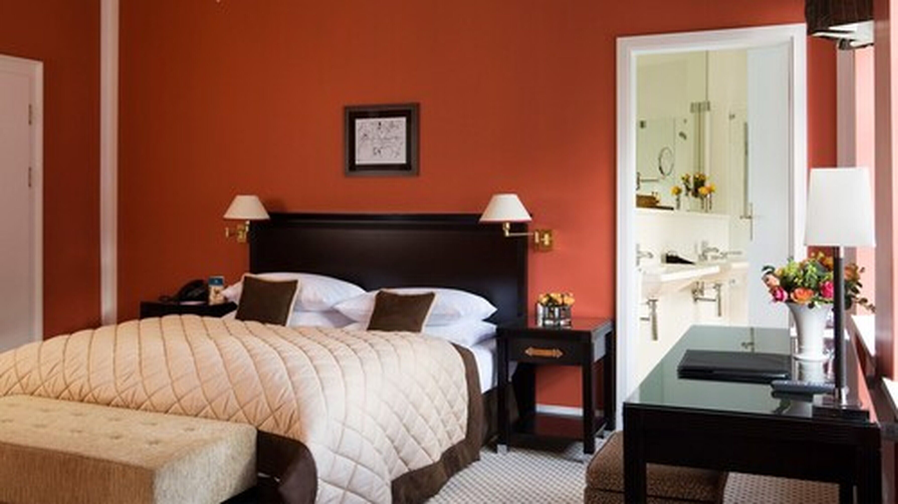 Una camera d'albergo con un letto grande, comodini, una scrivania e un bagno visibile attraverso una porta aperta.