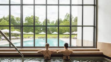 Two people in a swimming pool with a view of a poolside area and umbrellas.