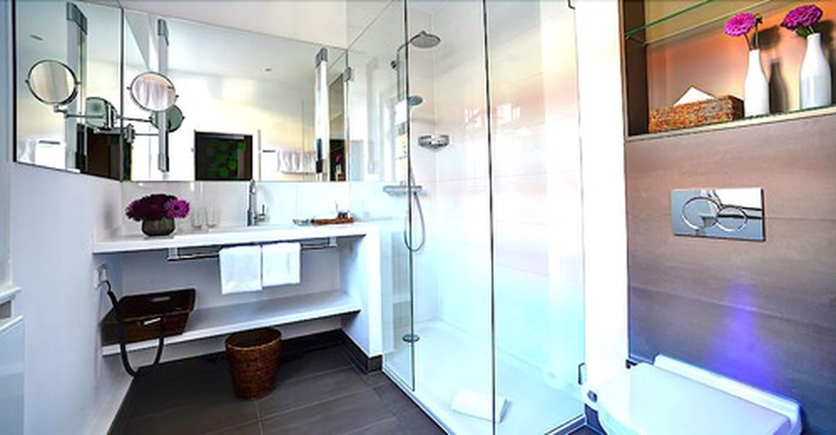 A modern bathroom with a glass shower enclosure, a white vanity with a mirror, and a small trash bin.