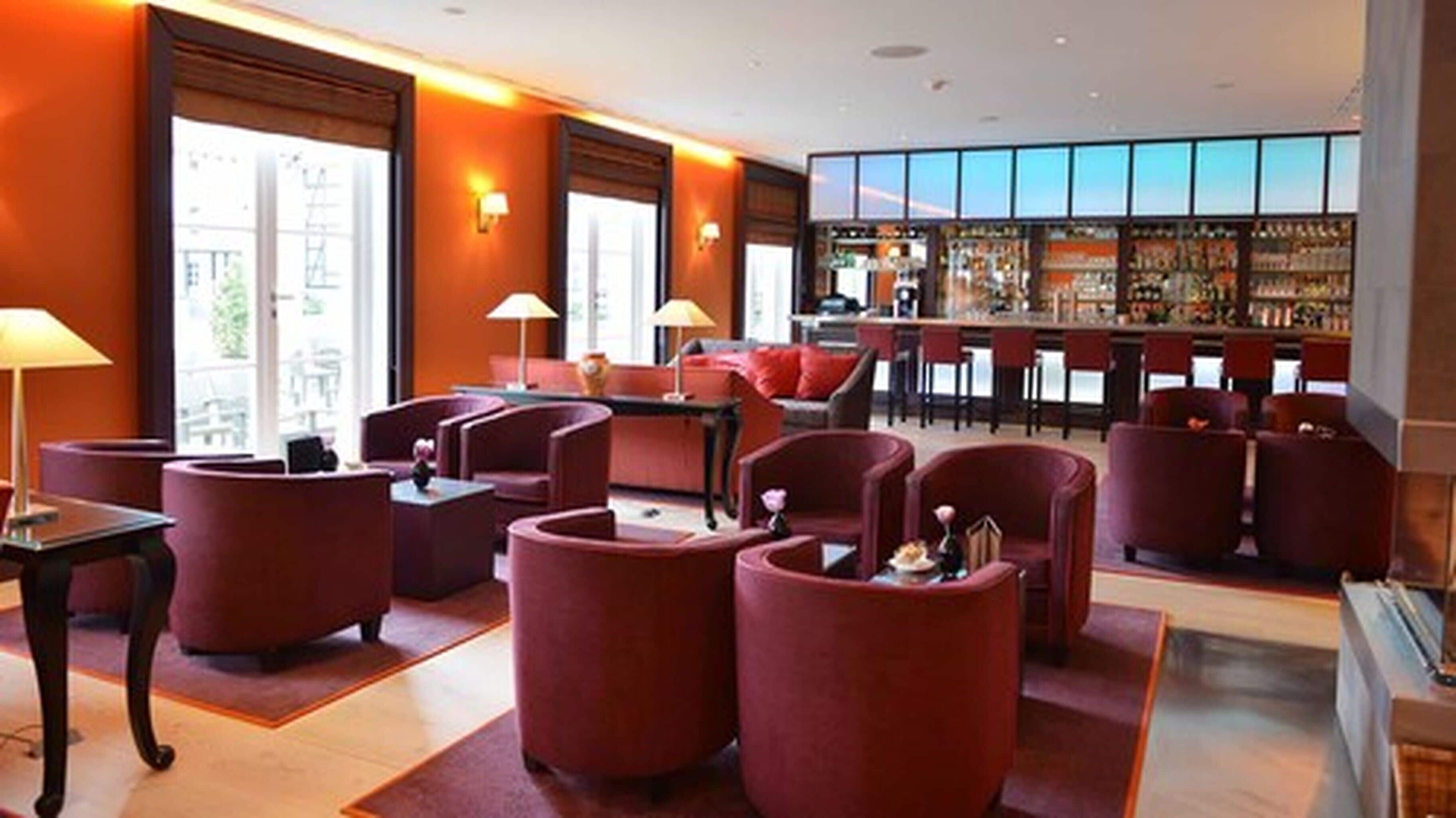 A hotel lobby with red seating, a bar area, and large windows.
