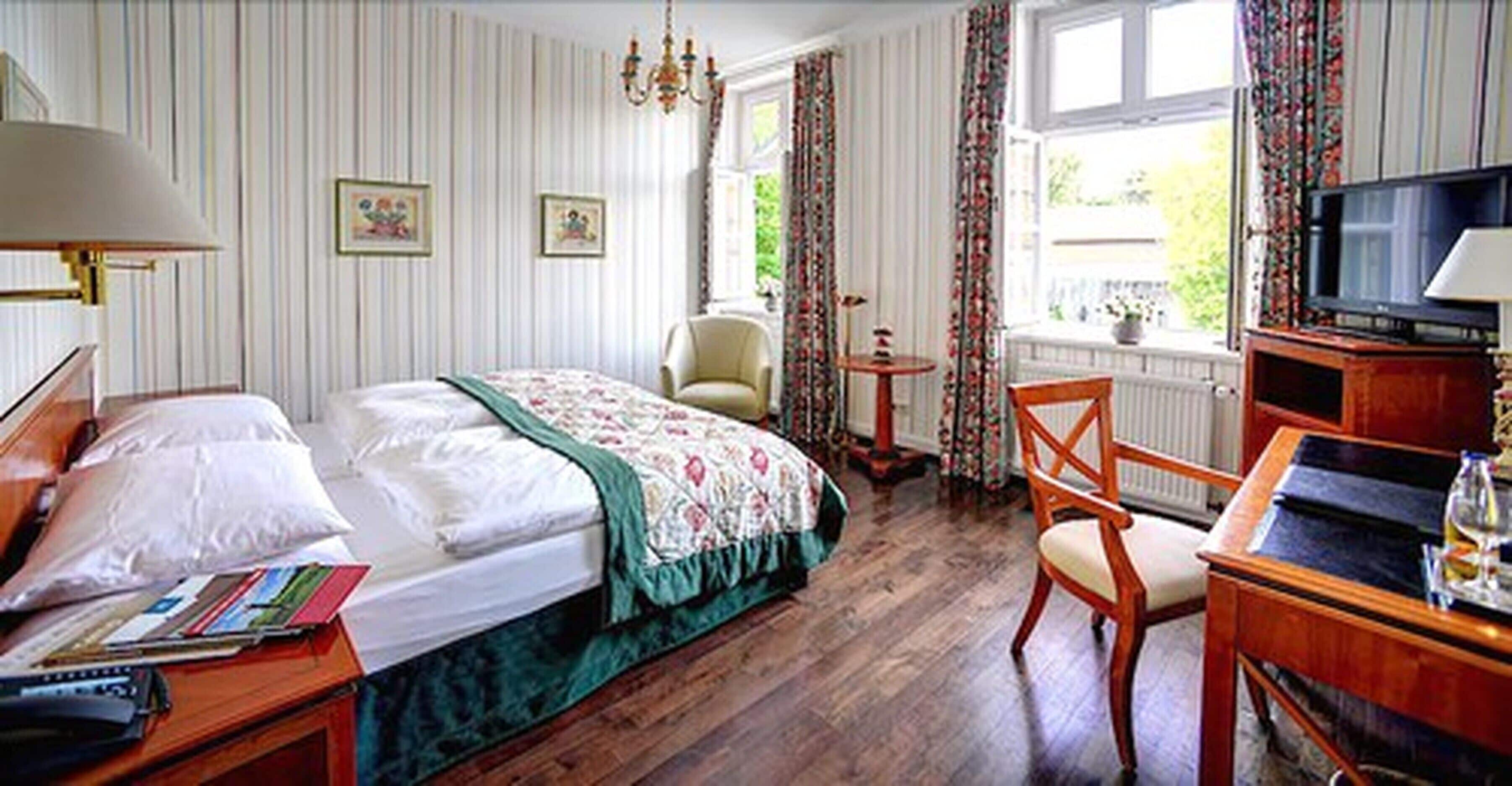 Une chambre d’hôtel avec un lit, un bureau avec une lampe, une chaise, une télévision et une fenêtre avec des rideaux.