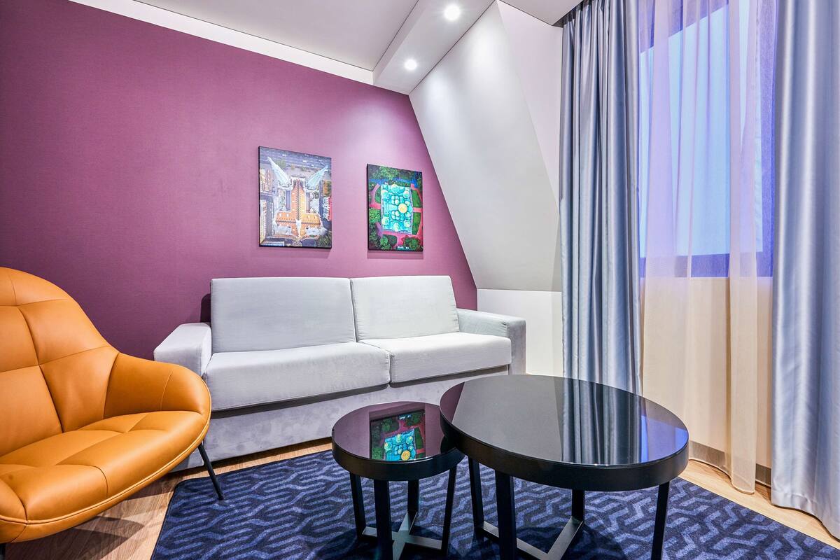 A modern room with a purple wall, a white sofa, an orange chair, and a round table.