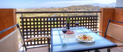 A balcony with a table set for two, featuring a bottle of wine, glasses, and plates of food.